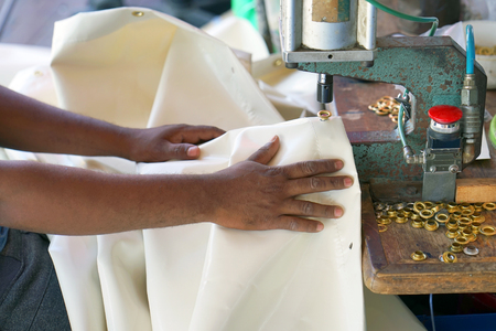 Men's African hands make holes in the tarpaulin. The seamstress sews a canvas on the sewing machine. Selective focus.の写真素材