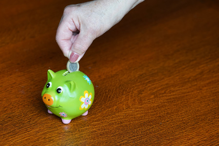 Hand of elderly puts money euro in her piggy bank. Closeup shot of the woman who puts a coin to the piggy bank. Savings, money, annuity insurance, retirement. Close-up. Copy space.の写真素材