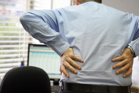 Close-up view of a office worker man with pain in kidneys. Young male with back ache clasping her hand to her lower back. Men suffering from ribbing pain, waist pain.の写真素材
