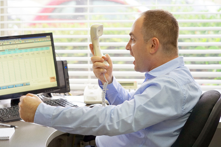 Close-up of an office worker swears with the client by phone. A man is shouting into the phone's phone. Funny facial expressions, emotions, reaction of perception, stress, gilding, nerves.の写真素材