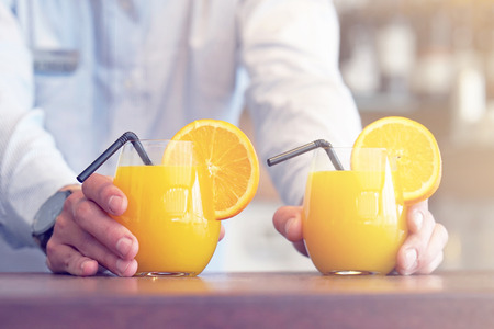 The barman gives two glasses of orange juice to the client of the hotel restaurant.の写真素材