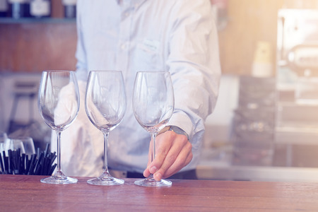 The bartender wipes the wine glasses. The waiter wipes the wine glasses. The bartender cleans the glass. Focus on the wine glasses. The concept of service. Toningの写真素材