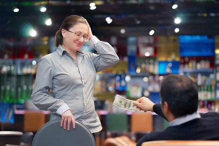 Waitress gets a tip from the client in the bar of the hotel. The girl in the vow. A bartender woman is happy to receive a tip at work. Shelves with bottles of alcohol in the background. Emotions.の写真素材