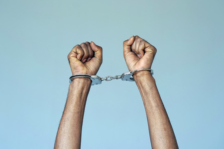 Close-up. Arrested african man handcuffed hands. Prisoner or arrested terrorist, close-up of hands in handcuffs. Isolated on gray backgroundの写真素材