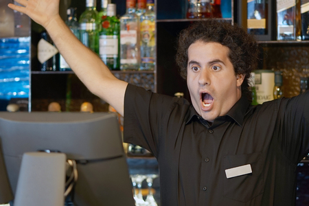 Male bartender made a mistake in the bill, emotion. A barmaid registrating new order by cash-register. A restaurant worker registrating new order by cash-register. The concept of service.の写真素材
