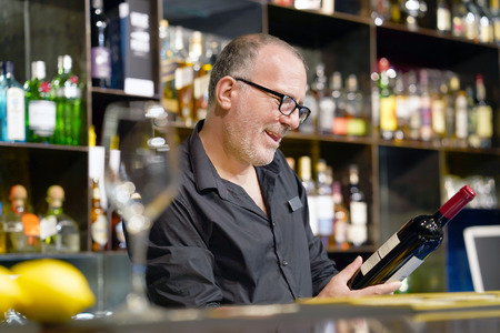 The barman is holding a bottle of red wine. The barman examines a bottle of red wine.の写真素材