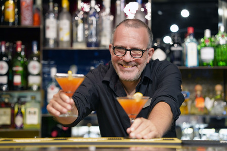 The barman gives a cocktail to the client of the hotel bar. Fresh cocktail. Alcoholic, non-alcoholic drink-beverage at the bar counter in the night club. Glass of grapefruit cocktail.の写真素材