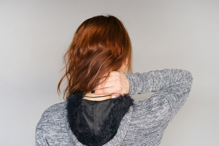 Close-up view of a young redhead woman with pain in the neck on gray background. Body And Health Care Concept.の写真素材
