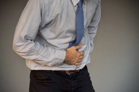 Man holding his stomach in pain isolated on gray background. Businessman suffering from abdominal pain. Body And Health Care Concept.の写真素材