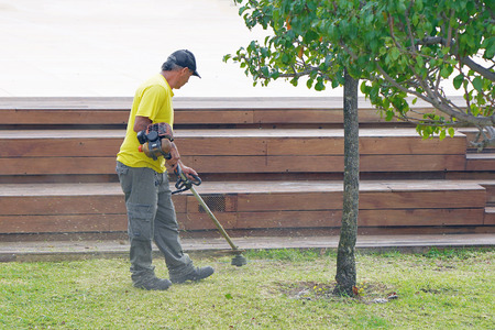 Professional gardener using an edge trimmer in the city parck. Elderly man worker mowing lawn with...