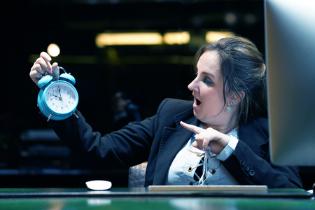 Woman holds an alarm clock in her hand in the workplace. female office worker holds an alarm clock in her hand at her desk. Woman holding a clock. Time management concept.の写真素材
