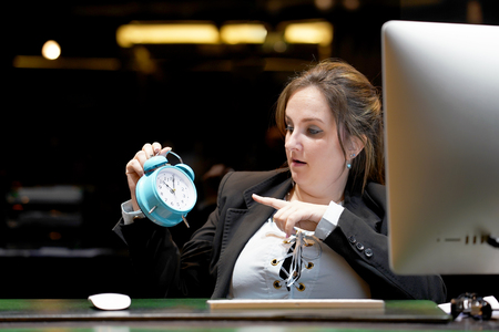Woman holds an alarm clock in her hand in the workplace. female office worker holds an alarm clock in her hand at her desk. Woman holding a clock. Time management concept.の写真素材