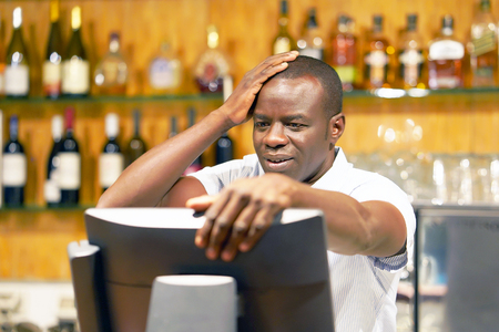 Male bartender made a mistake in the bill, emotion. A barmaid registrating new order by cash register. A restaurant worker registrating new order by cash register. The concept of service.の写真素材