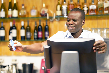 The barman gives the card to the client. Registration male of bartender employee of a new order by a cash register. The barman pays the order with a credit card. Service concept.の写真素材