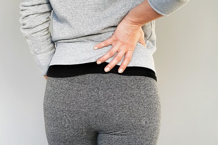 Young woman with back ache clasping her hand to her lower back. Close-up view of a young woman with pain in kidneys isolated on a gray background. Woman suffering from ribbing pain, waist pain.の写真素材