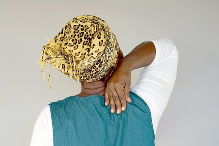 African elderly woman in scarf with pain in her back isolated on a gray backgroundの写真素材
