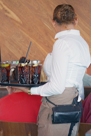 The waitress is carrying drink to the clients of the restaurant. Waitress serving a clients sitting...