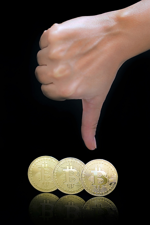 Female arm show thumb down sign. Thumb down hand sign. Close-up golden virtual currency bitcoin isolated on black background. Physical Bitcoin. Crypto currency trading concept.の写真素材
