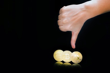 Female arm show thumb down sign. Thumb down hand sign. Close-up golden virtual currency bitcoin isolated on black background. Physical Bitcoin. Crypto currency trading concept.の写真素材
