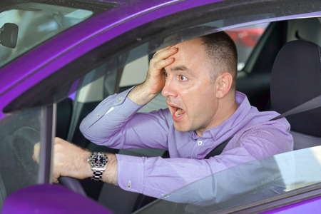 Side window view of inexperienced anxious motorist. Man driving a violet car shocked about to have traffic accident, windshield view. Scared funny looking young man driver in the car.の写真素材