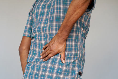 Close-up african man with pain in kidneys isolated on a gray background. Elderly man with back ache clasping her hand to her lower back. Man suffering from ribbing pain, waist pain.の写真素材
