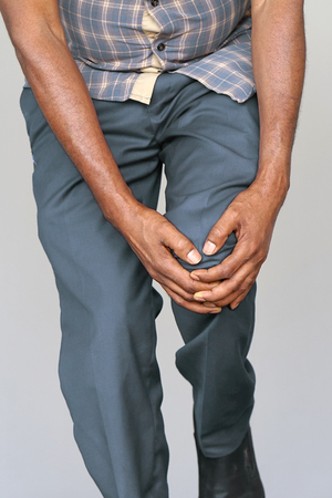 Pain In Knee. Close-up old African Male Leg With Painful Kneeson isolated on a gray background. Elderly man Feeling Joint Pain, Having Health Issues And Touching Leg With Hands. Health Care Concept.の写真素材