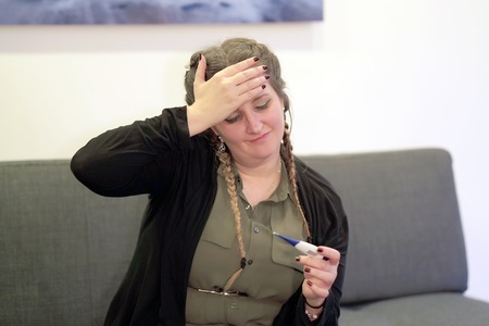 Woman holding thermometer in hands, measuring body temperature while suffering from influenza....