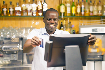 The barman gives the card to the client. Registration male of bartender employee of a new order by a cash register. The barman pays the order with a credit card. Service concept.の写真素材