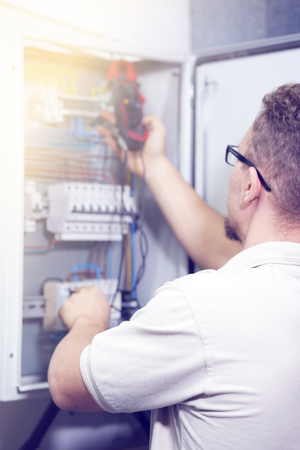 Electrician male measures voltage with multimeter in electrical cabinet. An electrician is checking the voltage in an electric box. Toningの写真素材