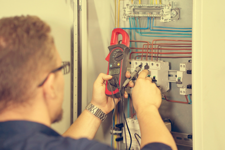 Electrician male measures voltage with multimeter in electrical cabinet. An electrician is checking the voltage in an electric box. Toningの写真素材