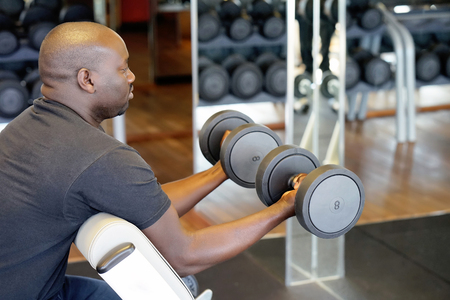 Hands of african man with dumbbells in the gym. Muscular man lifting a dumbbells on bench at gym, side viewの写真素材