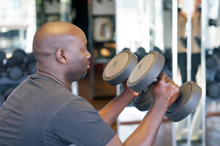 Hands of african man with dumbbells in the gym. Muscular man lifting a dumbbells on bench at gym, side viewの写真素材