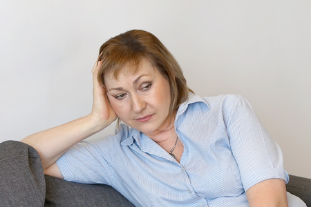 Elderly woman suffering from headache migraine pain at home. Health problem, stress and depression. Female holds head with hand. Concept of health.の写真素材