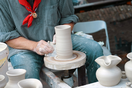 Close-up hands male creating cans or vases of gray clay. Man's hands make a clay pitcher, macro. Potter makes a pitcher.の写真素材