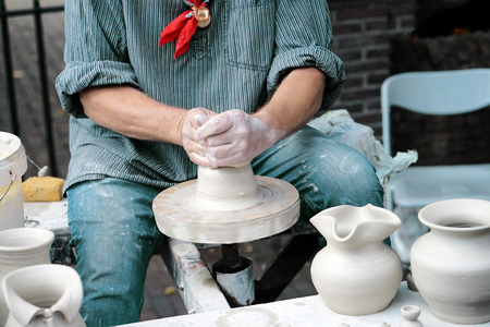 Close-up hands male creating cans or vases of gray clay. Man's hands make a clay pitcher, macro. Potter makes a pitcher.の写真素材