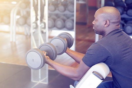 Hands of african man with dumbbells in the gym. Muscular man lifting a dumbbells on bench at gym, side view. Toningの写真素材