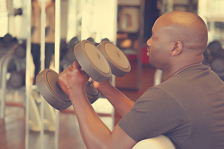 Hands of african man with dumbbells in the gym. Muscular man lifting a dumbbells on bench at gym, side view. Toningの写真素材