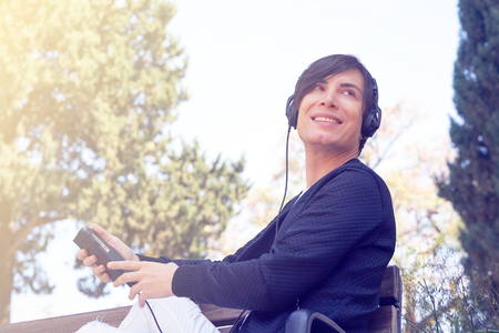 Joyful attractive guy listening to music on headphones enjoying in the park. Happy man listening to music from a smart phone with a against the bright sun. Toningの写真素材