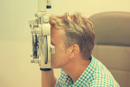 health care, medicine, people, eyesight and technology concept - Male checks his vision on the machine checking patient vision at eye clinic or optics store. Face close-up. Toningの写真素材