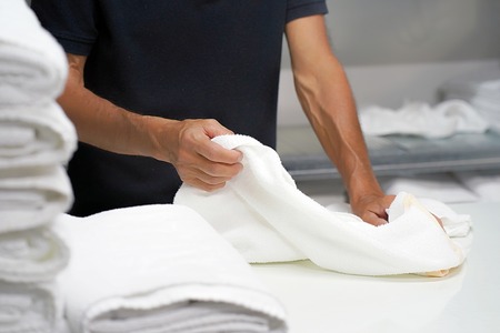 Hands of caucasian male laundry hotel worker folds a clean white towel. Hotel staff workers. Hotel linen cleaning services.の写真素材