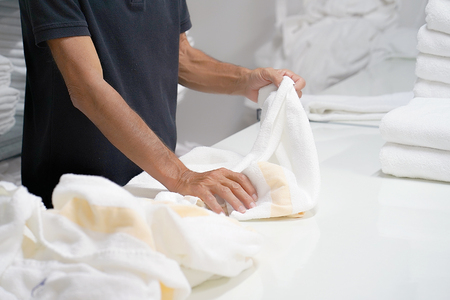 Hands of caucasian male laundry hotel worker folds a clean white towel. Hotel staff workers. Hotel linen cleaning services.の写真素材