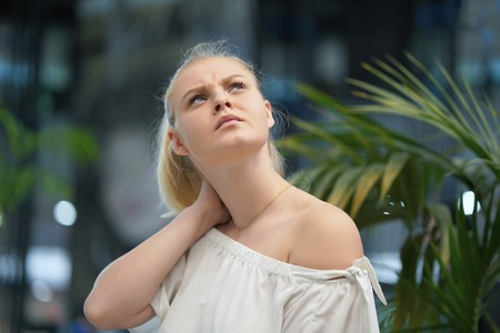 Tired neck. Young girl suffering from neck pain. A woman's sense of fatigue, exhausted, stressed. A girl massages her painful neck with her hands. The concept of body and health.の写真素材