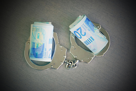 roll Israeli money bills (banknotes) of 200 shekel in handcuffs. Shekel bills with handcuffs. Handcuffs and money on table. Financial crime, dirty money and corruption concept. Tax offense conceptの写真素材