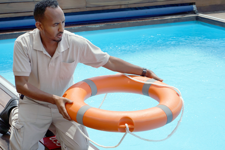 Hands of the rescuer with lifebuoy in pool. Hotel worker throws a lifeline to a drowning pool. Salvation of a sinking person. Life ring in swimming pool. Red lifebuoy pool ring.の写真素材