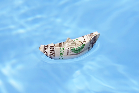 A boat out of the dollar in blue water. A boat made of paper money in blue water close-up. Concept...