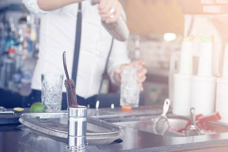 A bartender stirring ingredients in a mixing glass in order to prepare and serve a chilled cocktail at a bar. The concept of service. Toning.の写真素材
