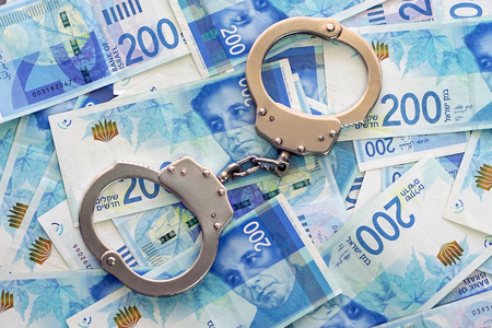 Handcuffs on the background of Israeli money. The new Israeli money bills (banknotes) of 200 shekel. Police handcuffs. Financial crime, dirty money and corruption concept.の写真素材