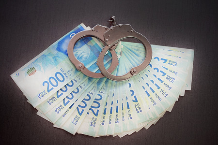 Handcuffs on the background of Israeli money. The new Israeli money bills (banknotes) of 200 shekel....