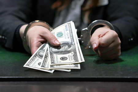 Woman in office in handcuffs holding a bribe of 100 dollars banknote. Arrested terrorist. Financial...