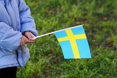 Hands of boy holding Sweden flag. Independence Day concept. Green grass background.の写真素材
